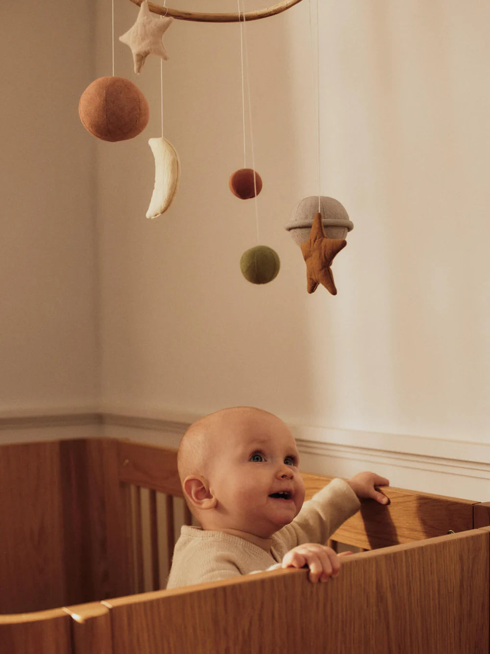 Baby steht im Kinderbett und schaut lächelnd zum Skye Mobile von Ferm Living hoch